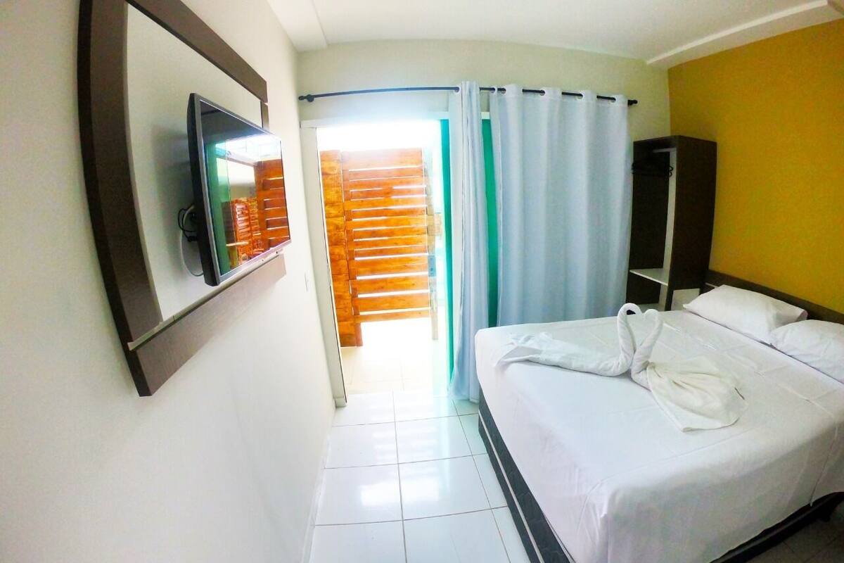 Habitación de hotel con cama, televisor, armario y baño visible a través de una puerta.