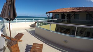A balcony with a view of the ocean, a wooden chair, and a table. - Pousada Porto Maraca (Ipojuca)