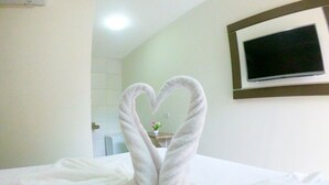 A hotel room with a bed, a heart-shaped towel arrangement, a TV mounted on the wall, and a small plant on a table. - Pousada Porto Maraca (Ipojuca)
