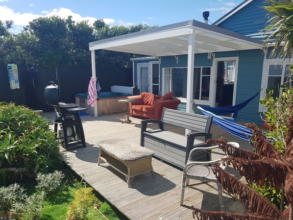 Un patio extérieur couvert équipé d’un barbecue, d’un espace salon avec un banc et des chaises, et d’un hamac.