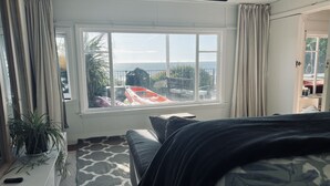 Une pièce avec une grande fenêtre, un lit, un tapis à motifs et une plante en pot.