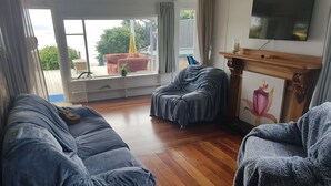 Un salon doté d’un plancher en bois, de deux canapés gris, d’un téléviseur fixé au mur et d’une fenêtre donnant sur un paysage verdoyant.