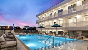 Un hôtel moderne doté d’une piscine, de chaises longues et d’un espace salon abrité.