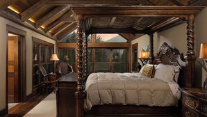A four-poster bed with a wooden canopy, a large window with a view of trees, and a wooden floor.