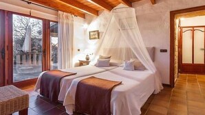 Une chambre avec deux lits, un plafond en bois, une porte vitrée donnant sur l’extérieur et un lit à baldaquin blanc.