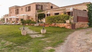 Un bâtiment rustique en pierre, doté d’un patio couvert, d’un espace extérieur aménagé pour s’asseoir et d’un chemin menant à l’entrée.