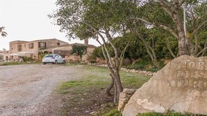 Une pancarte en pierre dont le texte est partiellement visible, une allée gravillonnée, une voiture garée et un bâtiment en arrière-plan.