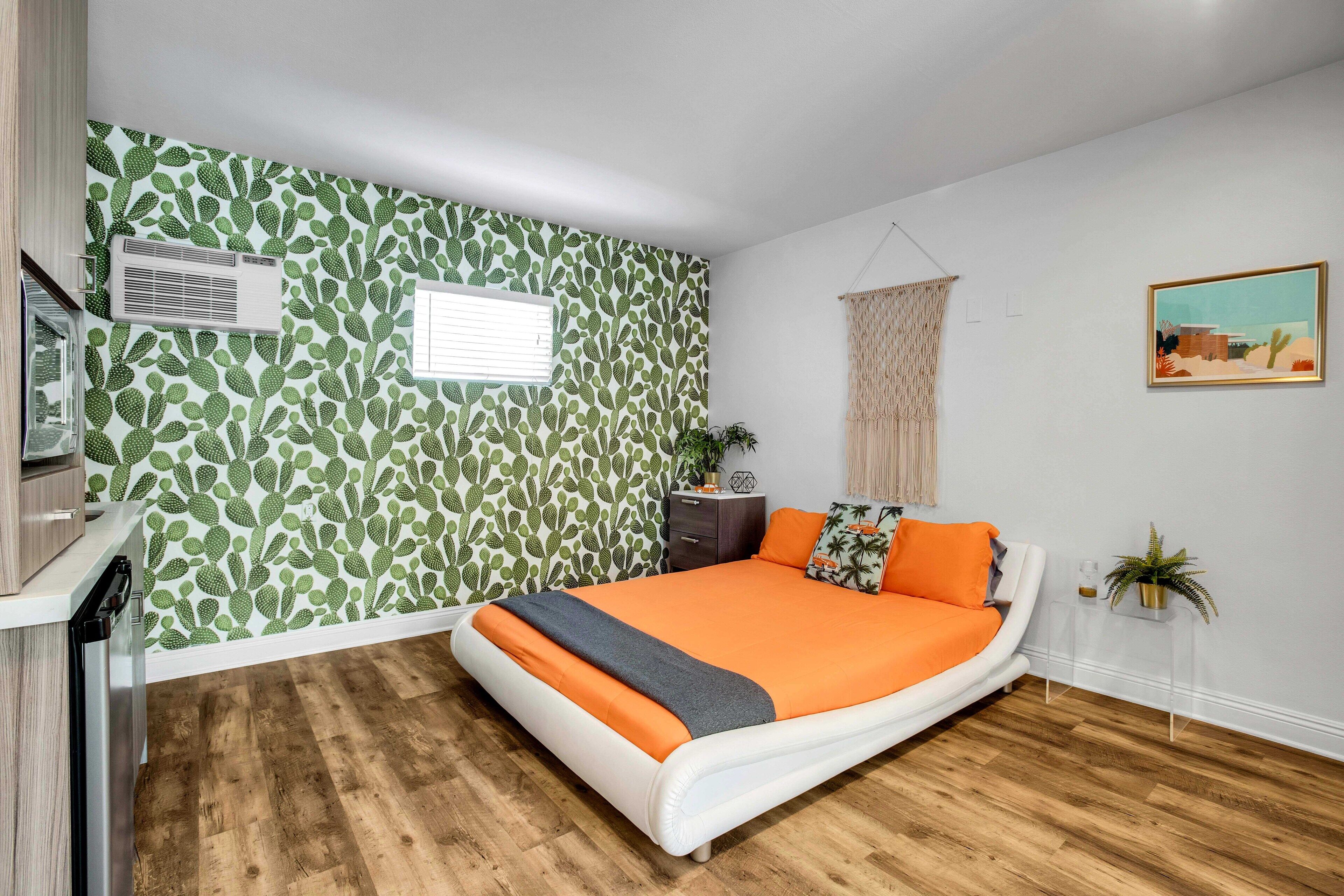 Ein Schlafzimmer mit Bett, Kommode, Klimaanlage, Fenster, Pflanze und einem Bild an der Wand.
