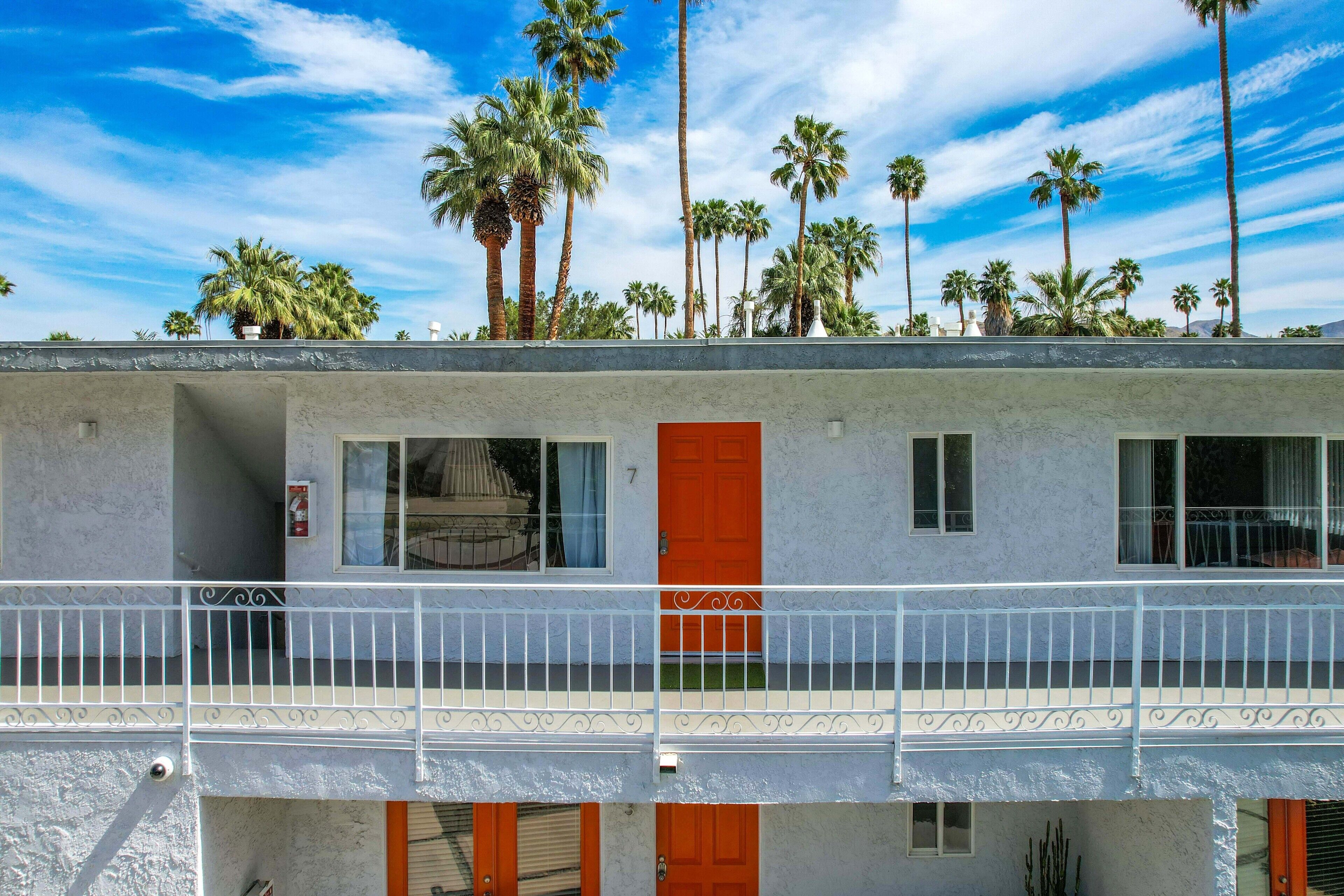 A two-story building with a balcony, a red door, and a view of palm trees.