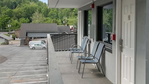 Un estacionamiento con varios coches, un edificio de fachada gris y una fila de sillas afuera.