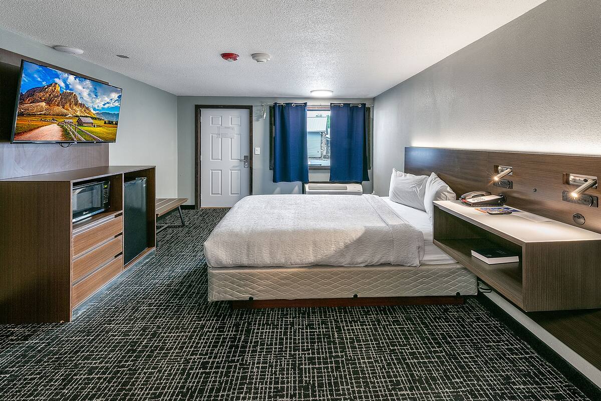 A hotel room with a bed, a desk, a TV, and a view of mountains through the window.