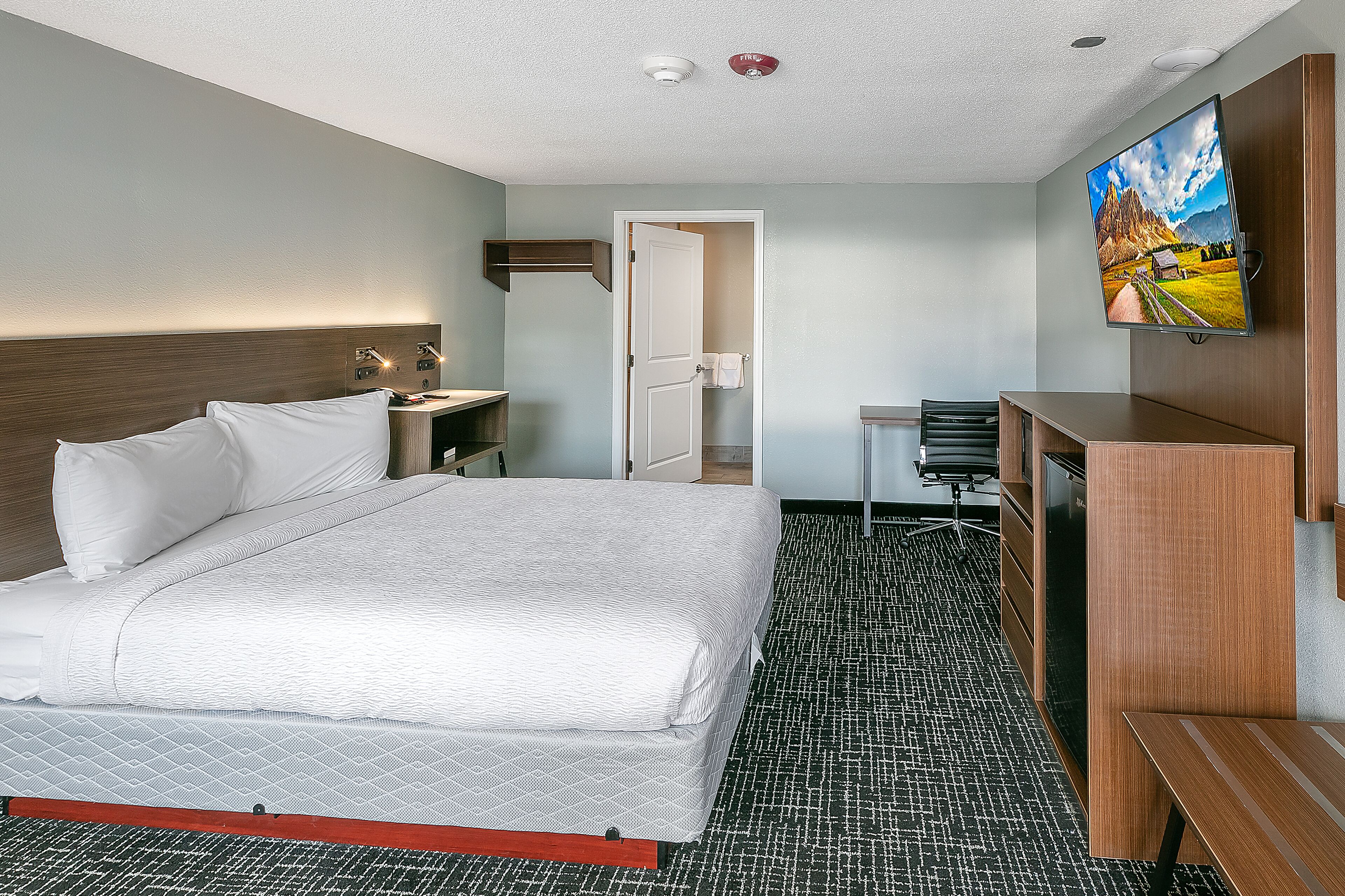 A hotel room with a bed, a desk, a TV, and a door leading to a bathroom.