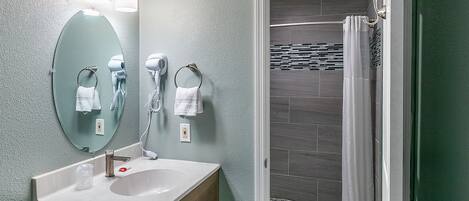 A bathroom with a sink, mirror, towel rings, and a shower area.