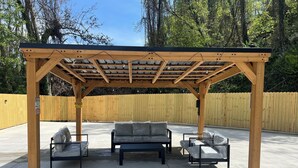 Una pérgola de madera con suelo de hormigón, rodeada por una valla de madera.