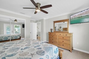 A bedroom with a bed, a dresser, a ceiling fan, and a TV mounted on the wall. - Extended Stays | Pet-Friendly | Steps to Beach | Pool (Destin)