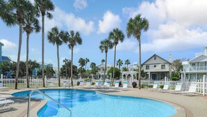 A swimming pool with lounge chairs and palm trees, surrounded by a fence and houses. - Pet-Friendly | Steps to Beach | Pool (Destin)