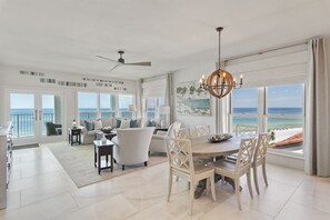 A spacious living area with a dining table and chairs, a ceiling fan, and a view of the ocean.
