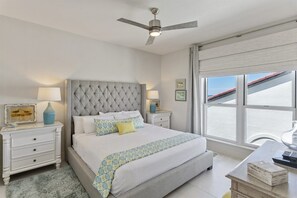 A bedroom with a tufted headboard, a bed with white linens, a bedside table with a lamp, and a view of the sea through a large window. - Grand Playa, Unit 402 | Gulf - Front Condo | Priva (Santa Rosa Beach)