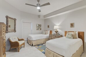 Una camera d'albergo con due letti, una poltrona, una cassettiera, una ventola a soffitto e opere d'arte alle pareti.