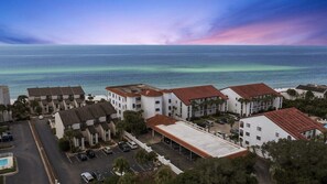 A coastal residential area with multiple two-story buildings, a parking lot, and a view of the ocean. - Grand Playa, Unit 402 | Gulf - Front Condo | Priva (Santa Rosa Beach)