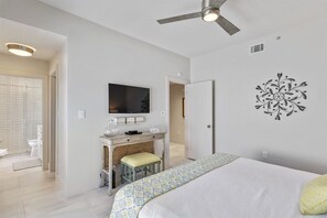 Une chambre à coucher comprenant un lit, un bureau, une télévision et un ventilateur de plafond.