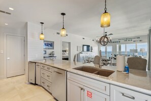 Una cocina moderna con una isla grande, iluminación colgante y vistas al océano.