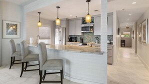 A modern kitchen with a central island, bar stools, pendant lighting, and a view into the adjacent dining area. - Grand Playa, Unit 402 | Gulf - Front Condo | Priva (Santa Rosa Beach)
