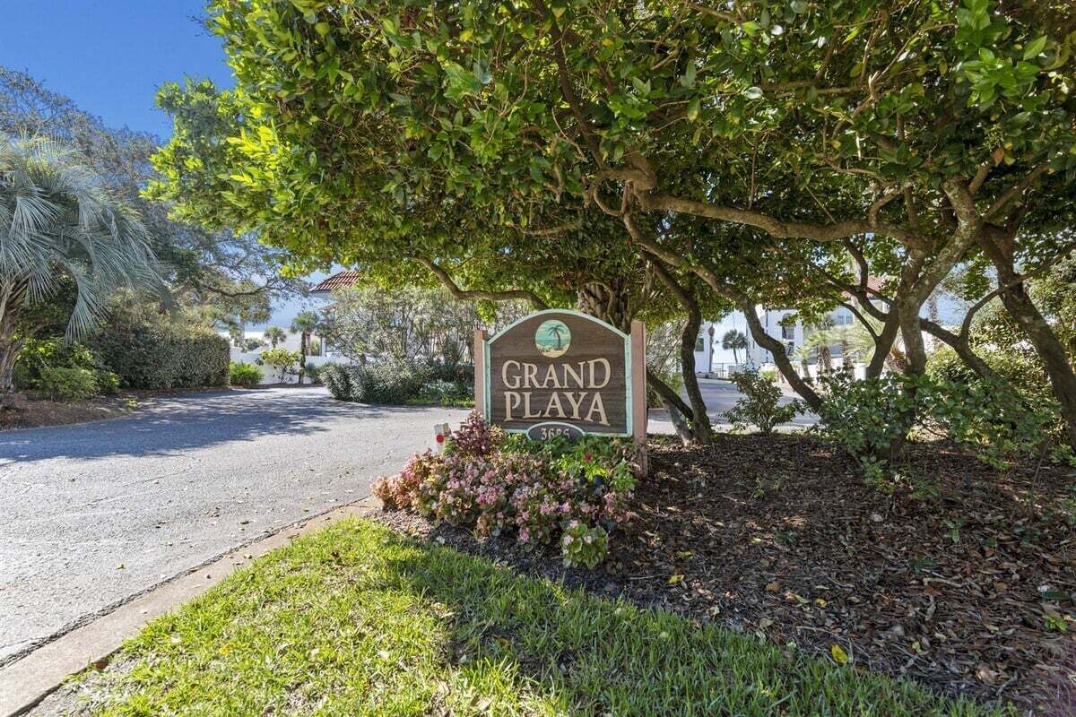 A sign for 'Grand Playa' with a view of a road and surrounding greenery.