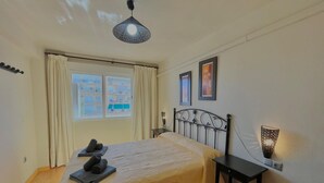 Ein ordentlich eingerichtetes Schlafzimmer mit einem Bett, einem Nachttisch, einer Hängeleuchte und einem Fenster mit Vorhängen.