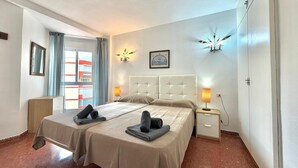 A hotel room with a bed, bedside tables, a nightstand, a mirror, a window with curtains, and wall-mounted lights. - TERRASOL PLAZAMAR 2-6 (Torre del Mar)