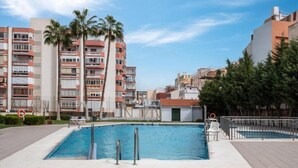 A swimming pool with a lifeguard chair, palm trees, and a multi-story building in the background. - TERRASOL PLAZAMAR 2-6 (Torre del Mar)