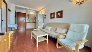 A living room with a sofa, armchairs, a coffee table, a TV, and a kitchen in the background. - TERRASOL PLAZAMAR 2-6 (Torre del Mar)