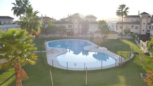 Una piscina rodeada por una valla, con palmeras y casas al fondo.