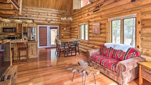 Ein Interieur einer Blockhütte mit einem Essbereich aus Holz, einer Couch mit gemustertem Überwurf und einem großen Fenster.