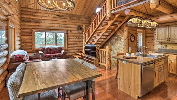 Ein Holzblockhaus-Interieur mit einem Holzesstisch, einer Couch, einer Treppe und einer Küchenzeile.