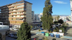 Ein mehrstöckiges Gebäude mit Balkonen, ein Parkplatz mit Autos und ein klarer, blauer Himmel.