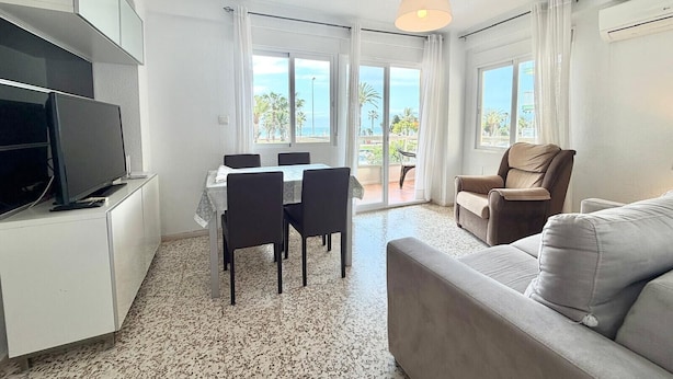 Ein modernes Wohnzimmer mit Flachbildfernseher, einer Couch, einem Esstisch mit Stühlen und einem Balkon mit Blick.
