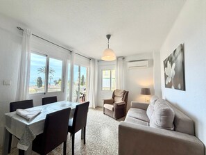 A room with a dining table, chairs, a sofa, a chair, a lamp, and a painting on the wall.