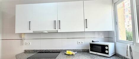 Cocina con armarios blancos, encimera de granito, microondas y fregadero.