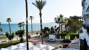 Vista de la playa con palmeras, una carretera y coches aparcados.