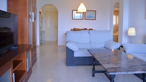 Una sala de estar con un sofá, una mesa de centro y un televisor. Se ve un pasillo que conduce a otra habitación.
