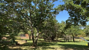 A park with trees, a playground, and a brick wall in the background. - Chacara Zabotto (São Carlos)