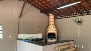 A kitchen with a brick oven, a wooden bench, and a fan on the wall. - Chacara Zabotto (São Carlos)