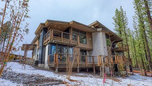 Een modern meerlaags huis met een balkon en grote ramen, omringd door bomen en sneeuw.