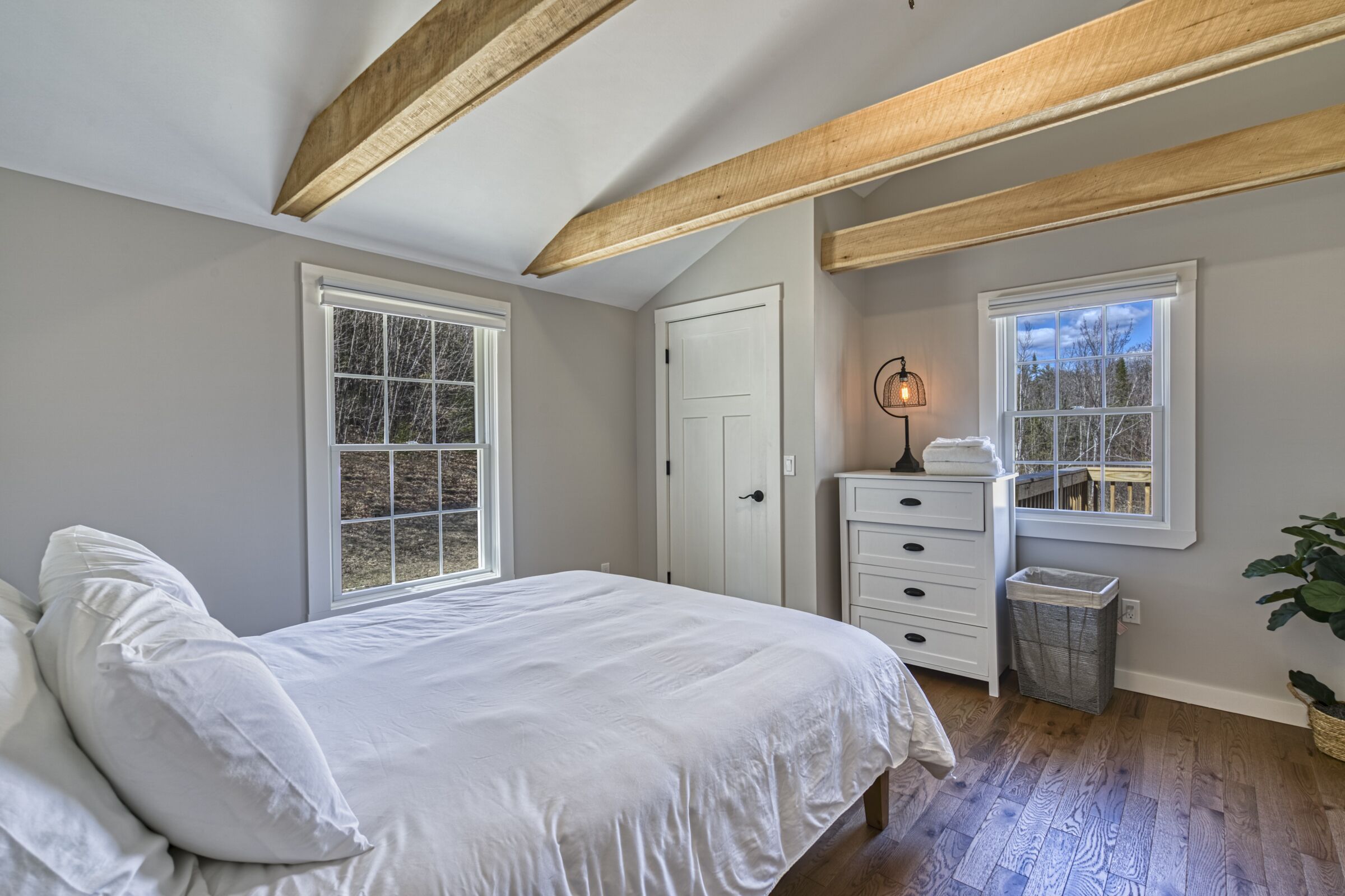 Une chambre à coucher avec un grand lit, deux fenêtres, une commode, une lampe et une poubelle.