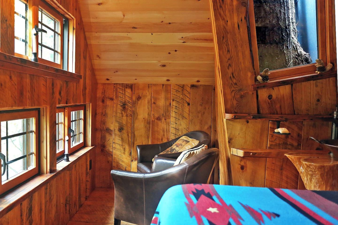Ein gemütliches Blockhaus-Interieur mit Holzwänden, einem Ledersessel, einem kleinen Tisch und einem Fenster mit Blick auf einen Baum.