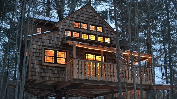 A wooden cabin with multiple windows and a balcony, surrounded by trees. - Tiffany Hill Treehouse by Sunapee Stays | Fireplace + Deck + Mount Sunapee (Newbury)