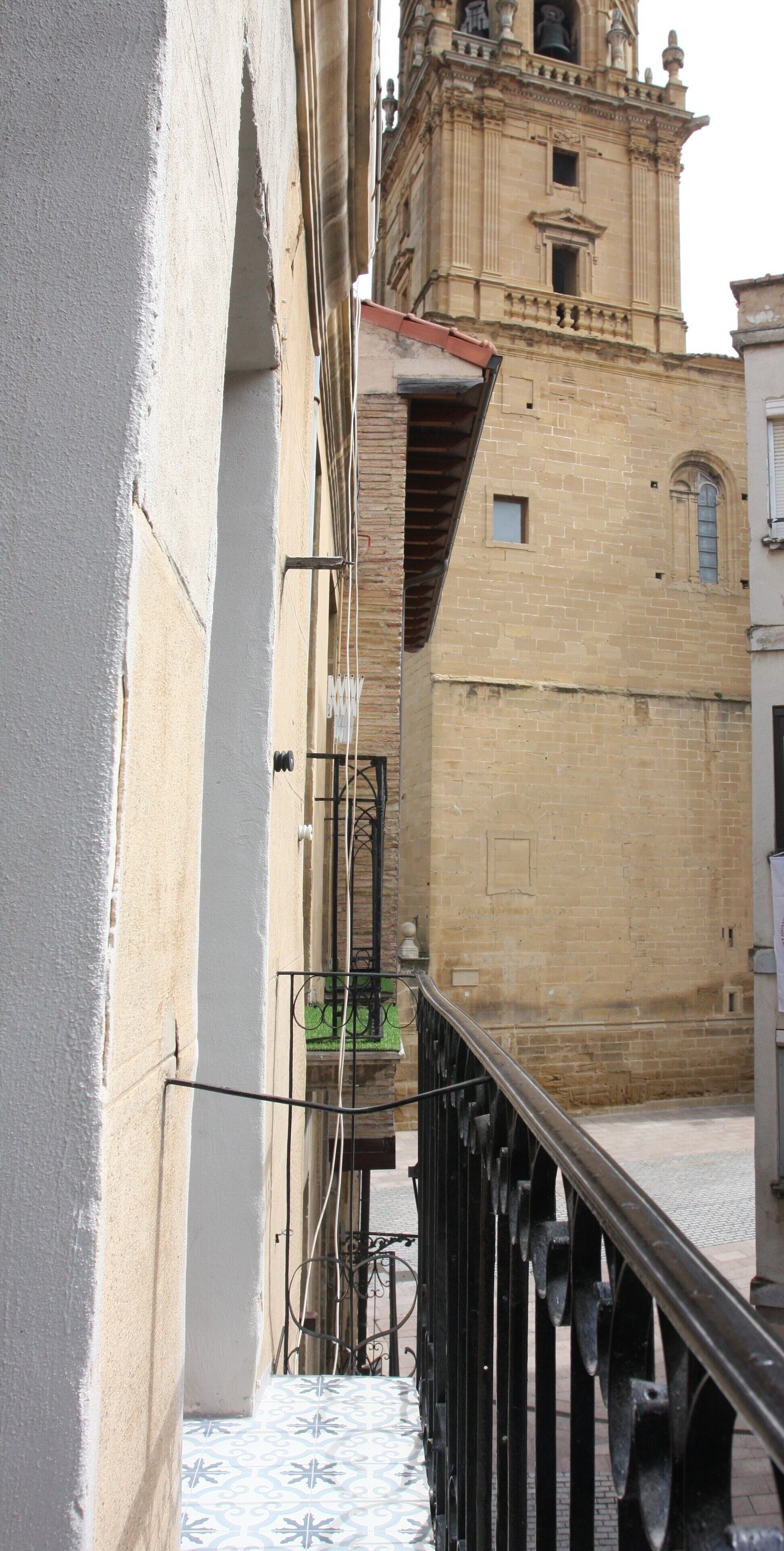 Una calle estrecha con un edificio que presenta una torre de campanas y un balcón con barandilla de metal.