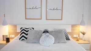 A modern bedroom with a bed, two framed wall art pieces, and a nightstand with a lamp and a vase. - Edificio Privado La Herradura (Haro)