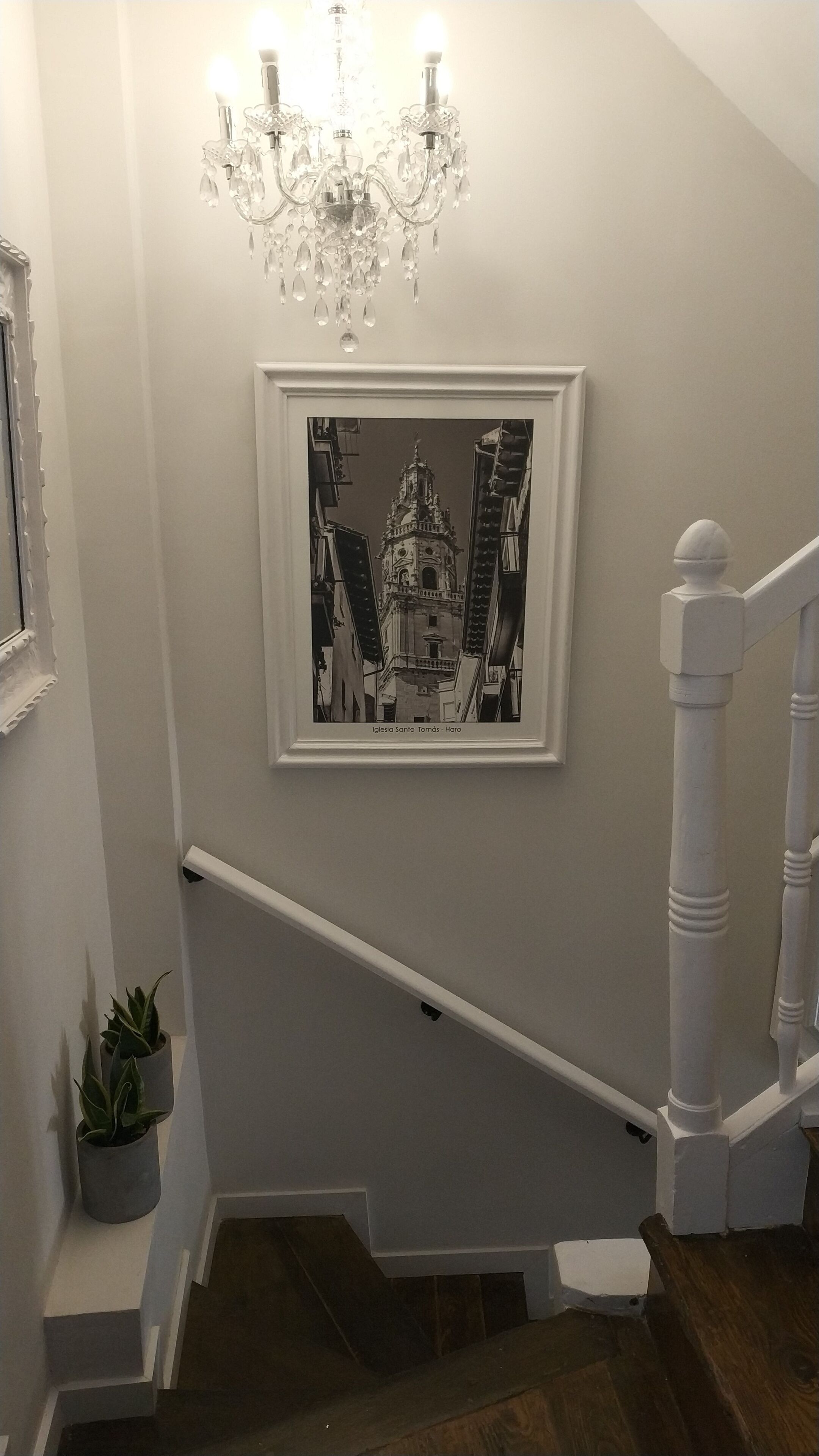 A staircase with a chandelier and a framed picture on the wall.